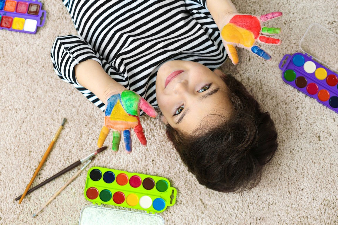 Kid laying on carpet with paint on hands